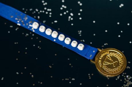 Close-up of a gold medal on a blue ribbon with 'possible' beading, symbolizing achievement.